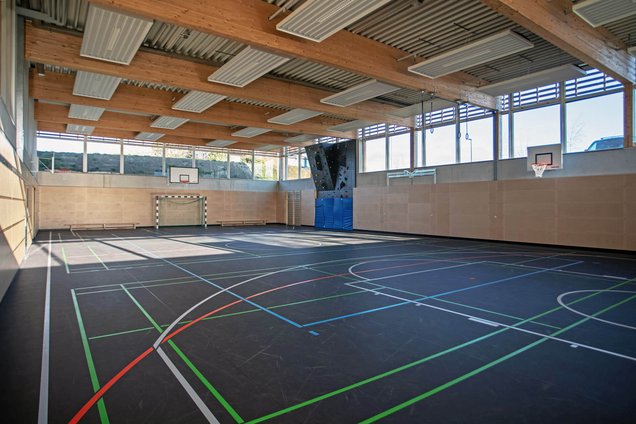 Blick in die moderne Turnhalle mit Kletterwand, Basketballkörben und Fußballtoren
